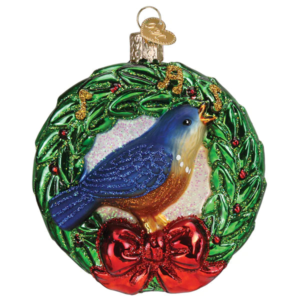 The Calling Bird Old World Christmas Ornament 16148 features a hand-painted bluebird on a green wreath with red berries, a red bow, sparkling glitter, and gold musical notes—a festive addition to your holiday décor.