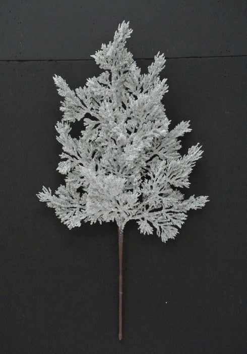 The 20 Green and White Snow Cedar Pick 23007 displays frosted green and white artificial branches with feathery offshoots, dusted in a snowy coating, set against a black background.