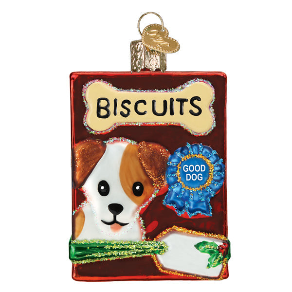 The Doggy Treats Old World Christmas Ornament 32585 is shaped like a red dog biscuit box with a cute cartoon dog, a “GOOD DOG” blue ribbon, bone-shaped “BISCUITS” label, and a green bow at the bottom.