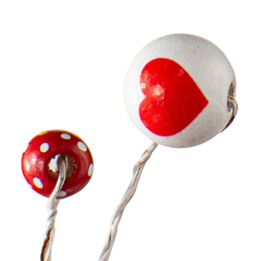 Close-up of two round beads on wires; the larger bead is white with a red heart design, and the smaller bead is red with white polka dots. Set against a bright, minimalist background, these beads charmingly echo the simplicity of the 28" Red and White Ball Spray 40045.