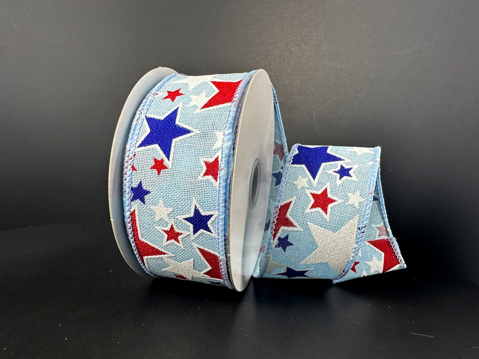 The 1.5X10Y Lt Blue Navy Red White Linen Glitter Stars Ribbon features red, white, and blue stars on a light blue background, elegantly coiled and perfect for adding sparkle and charm to any decor with its wired star pattern against a dark surface.