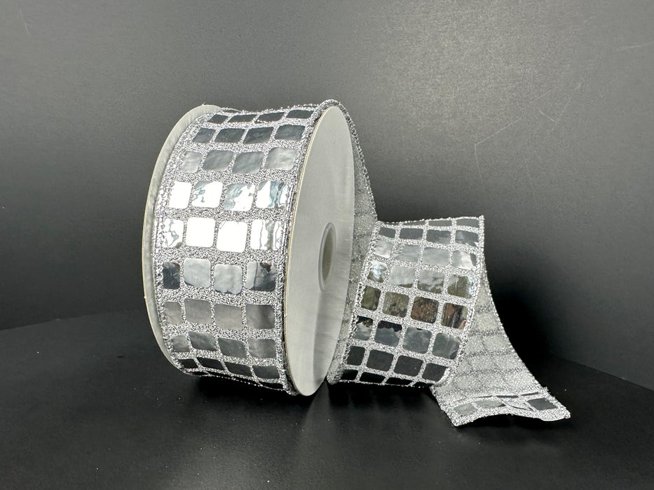A partially unrolled 1.5X10Y Silver Discoball Sequins Ribbon, featuring a silver grid pattern of reflective squares and wired edges, sits on a dark surface—perfect for adding sparkle to any project.