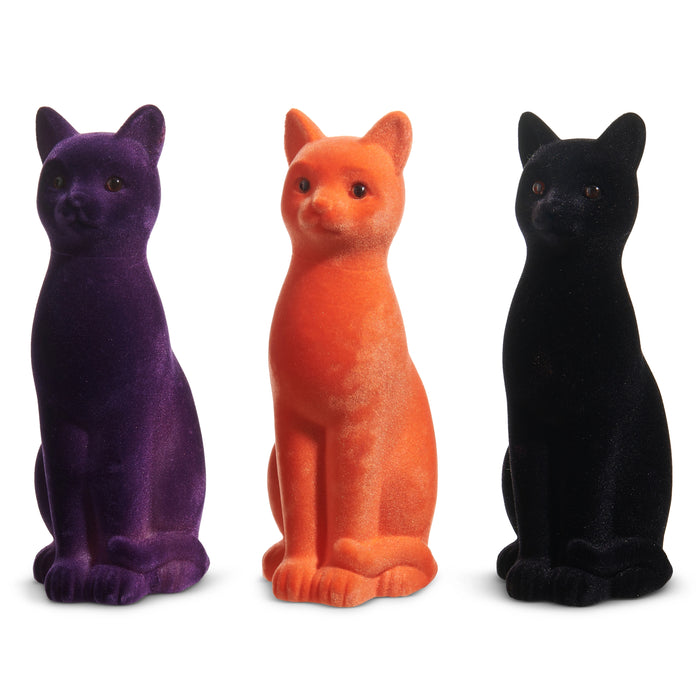 Three 11" Flocked Cat figurines (4540848) in purple, orange, and black sit upright side by side. Each features a plush velvet texture—perfect for adding a festive touch to your Halloween decor.