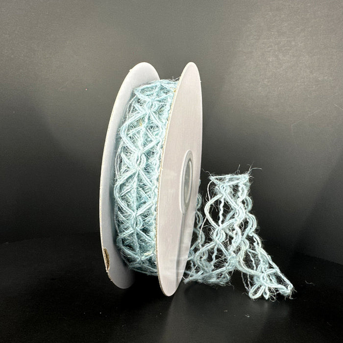 A spool of 7/8X10Y Lt Blue Scallop Weave Burlap Ribbon (67348-05-05) stands upright against a dark background. A loose section elegantly drapes to the side, highlighting its delicate pattern.