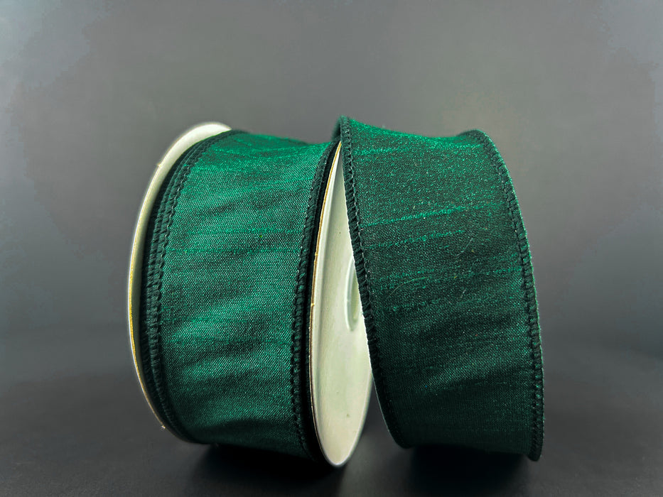 Two rolls of the 1.5"x10Y Hunter Green Faux Dupioni Ribbon stand out against a neutral gray background. The satin-finish ribbons are neatly wound on white spools, highlighting their thin black edges, and bring an elegant touch with their wired structure for easy shaping.