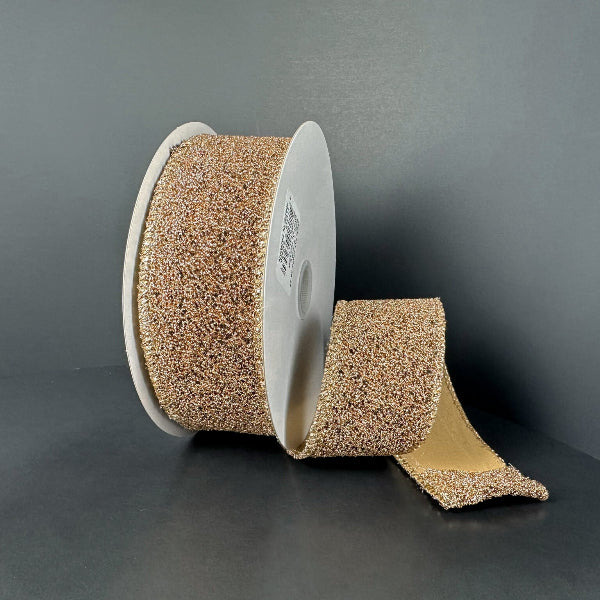 A large roll of 1.5X10Y Toffee-Black Fuzzy Metallic Ribbon (73566-09-35) is displayed on a white spool, with part of the strip unrolled and laying flat against a dark surface—resembling an industrial toffee ribbon.