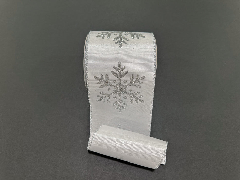 A 4X10Y White Ribbed Satin/Silver Giant Glitter Snowflake Ribbon (73569-04-16) with shimmering snowflake designs lies on a plain dark background.