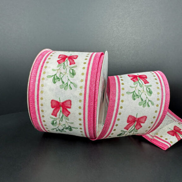 A spool of 2.5X10Y Ivory Linen/Mistletoe Bow/Pink Edge Ribbon 76502-40-44, with red bows and green leaves on white and pink edges, is displayed on a dark surface—perfect for adding festive charm to your decor.