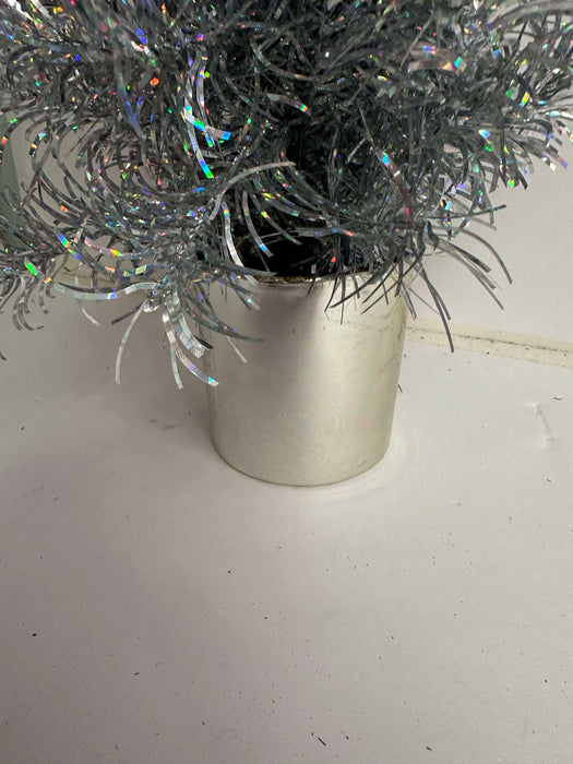 A close-up of the 24 In Tinsel Tree 84578-Silver with shimmering branches in a metallic silver pot, displayed on a white surface.