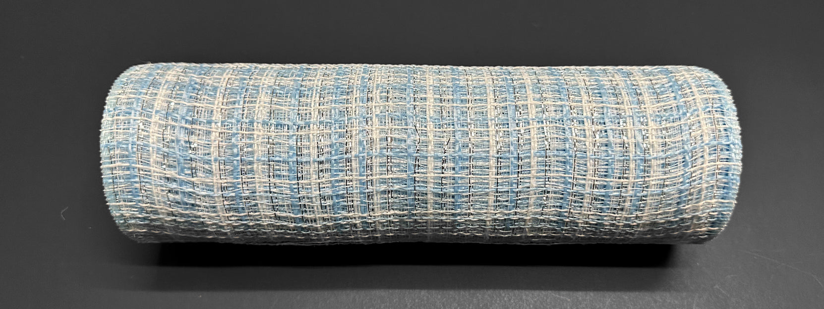 The product "10\"X10Y Lt Blue-White-Silver Metallic Tweed Mesh XB235710-04" is a cylindrical, textured object resembling a fabric roll, showcasing a woven pattern in metallic tweed with light blue and off-white threads that subtly glimmer on its dark surface.