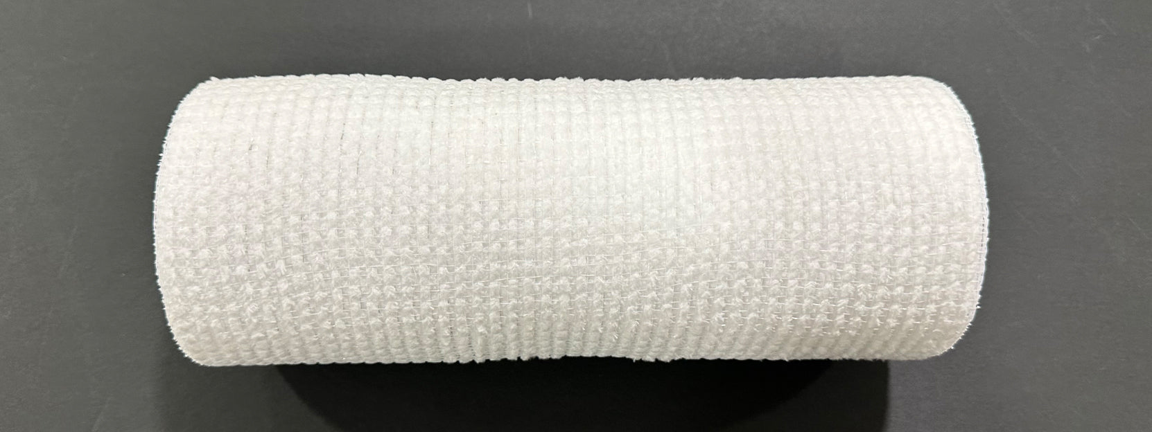 A close-up of the 10X10Y White All Snow Fuzz Mesh XB253610-01 medical bandage roll, showcasing its textured surface against a black background.