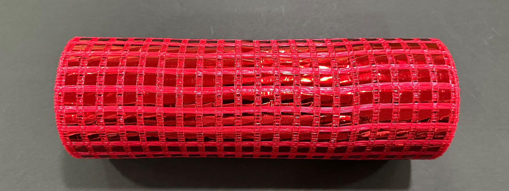 A 10X10Y roll of red metallic wide mesh (XB254110-12) with a grid pattern is displayed on a plain dark surface, highlighting its shiny metallic texture.