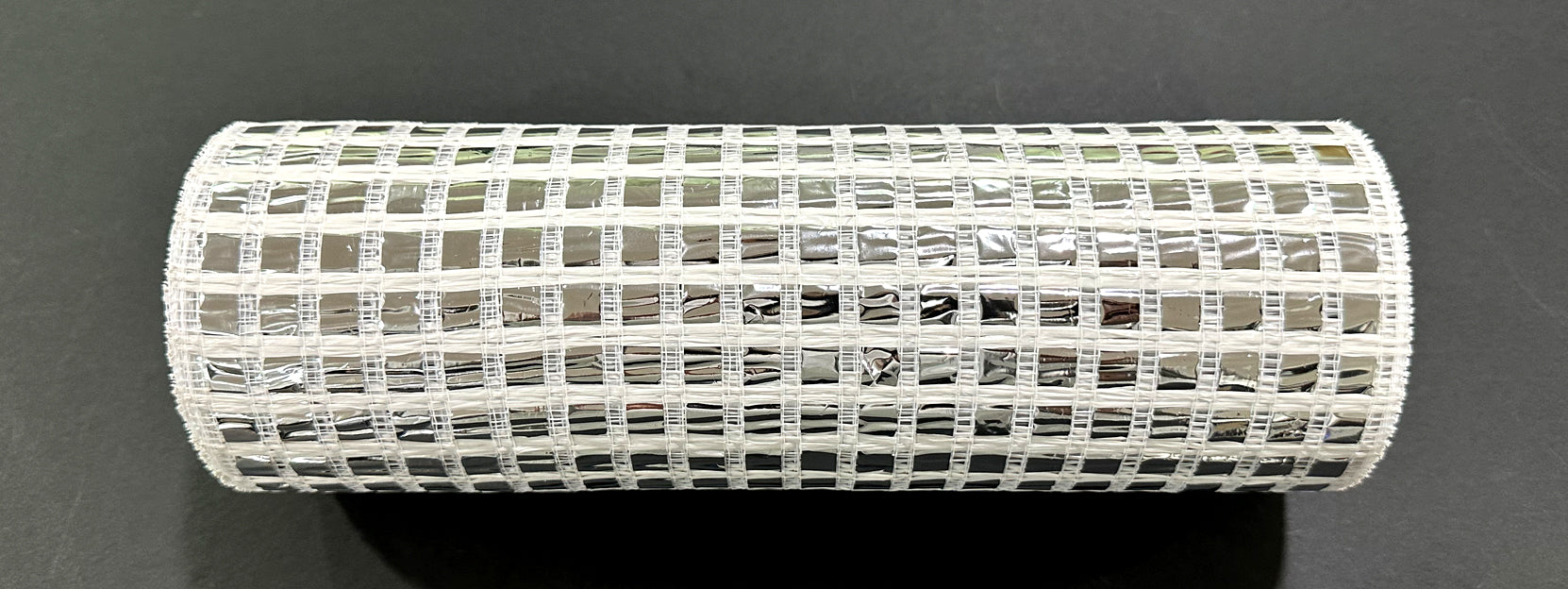 A roll of 10X10Y Silver Metallic Wide Mesh (XB254110-51) with a grid pattern and silver sheen rests on a black surface.