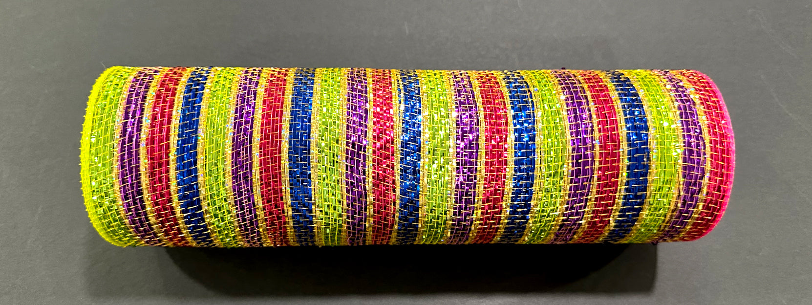 A 10X10Y cylinder wrapped in Purple-Red-Royal-Lime-Gold Metallic Stripe Mesh (XB254310-11) sits on a dark, flat surface.