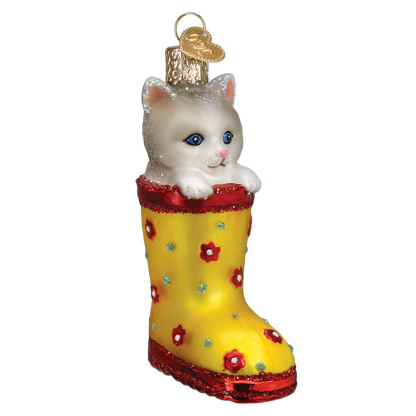 The Kitten In Rain Boot Ornament by Old World Christmas (12606) features a white kitten with blue eyes peeking from a yellow boot with red and blue flowers, finished with a gold hanging loop—an adorable accent for any space.