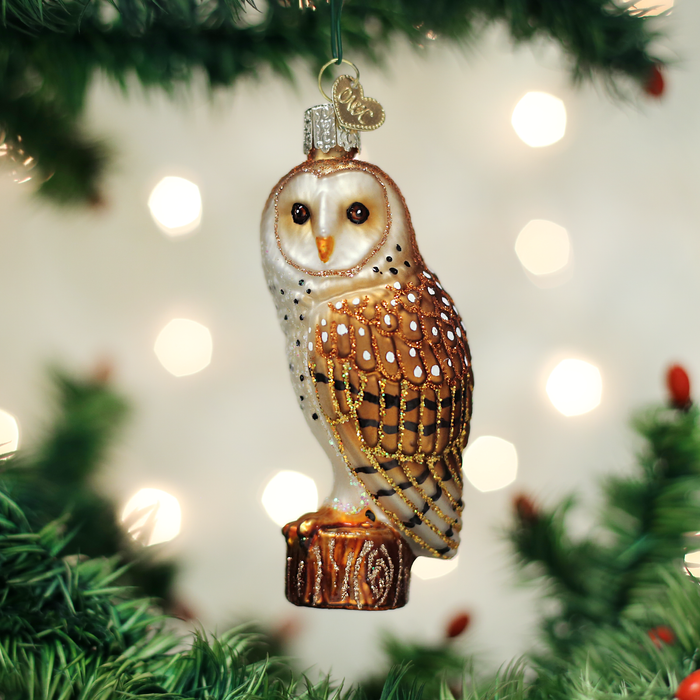 The Barn Owl Ornament Old World Christmas Ornament 16118, with brown and white detail, hangs among green pine needles and blurred holiday lights, capturing festive charm for your tree.