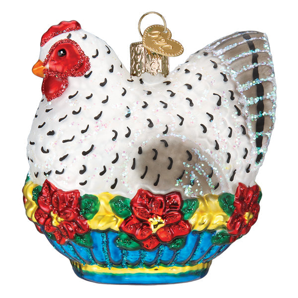 The French Hen Ornament by Old World Christmas (16144) features a white hen with black spots, red comb, and flowers, sitting in a blue basket with yellow and green accents. Includes a gold loop for hanging. Inspired by the Twelve Days of Christmas.