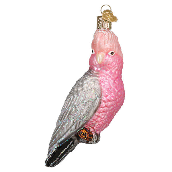 The Rose-breasted Cockatoo Ornament by Old World Christmas (16146) is a glass piece shaped like a rose-breasted Galah, featuring vibrant pink and gray colors with sparkling accents, perched with a gold cap for hanging.