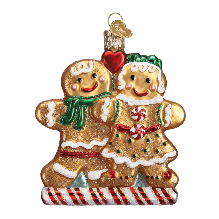 The Gingerbread Friends Ornament (Old World Christmas Ornament 32219) features two smiling figures, one with a green scarf and one with a green bow, holding a red heart on a striped candy base.