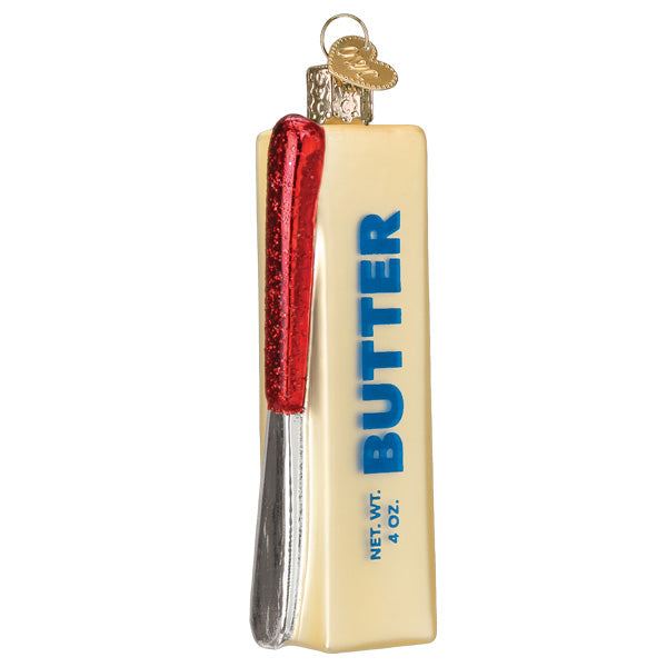 The Stick Of Butter Ornament by Old World Christmas (32510) is a glass Christmas tree ornament shaped like a butter stick with a red and silver knife, featuring “BUTTER” and “NET WT. 4 OZ.” in blue—just like Grandma’s kitchen!.