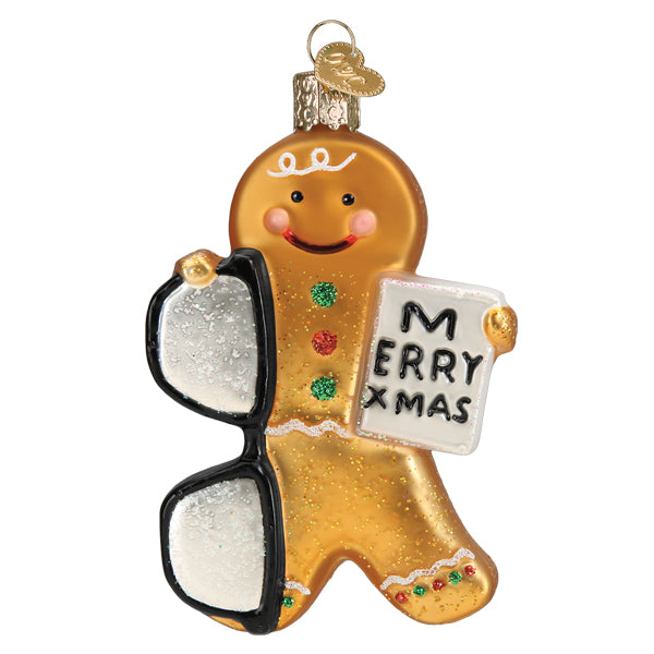 The Gingerbread Optometrist Ornament by Old World Christmas (32539) features a smiling cookie holding black glasses and a "MERRY XMAS" sign, decorated with colorful icing—a perfect glasses-themed addition to your tree.