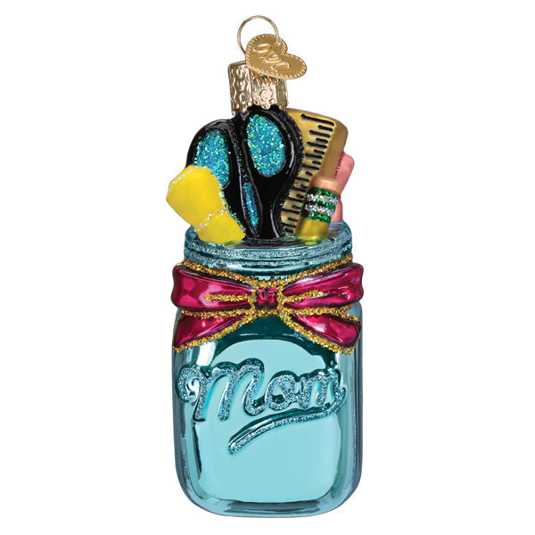 The Homeschooling Mom Ornament from Old World Christmas (32541) is a shiny blue mason jar labeled "Mom," filled with glittery craft supplies and topped with a pink bow and gold cap—perfect for celebrating homeschool moms.