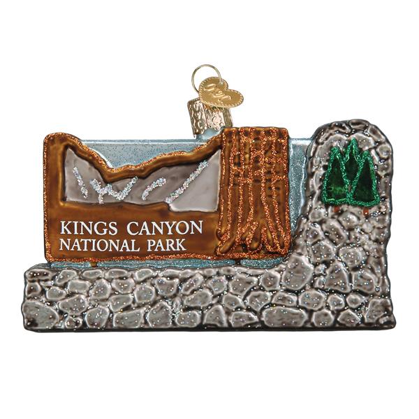 The Kings Canyon National Park Ornament by Old World Christmas (36283) features a brown wood sign with a rock base, mountain design, and green tree, topped with a gold cap for hanging—a unique holiday decoration.