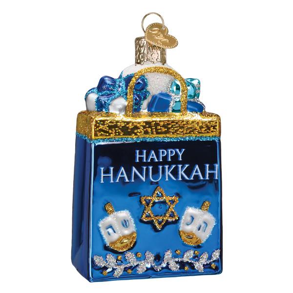The Happy Hanukkah Old World Christmas Ornament 36302 is a hand-painted glass decoration shaped like a gift bag, featuring “Happy Hanukkah,” a Star of David, dreidels, and blue and white presents.