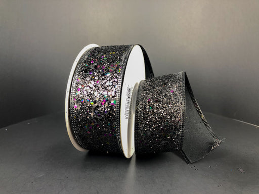 A spool of Black Super Glitter, 1.5X10Y Ribbon (75102-09-21) rests on a dark surface, with some ribbon unrolled to display its sparkling multicolored glitter and shiny, textured finish.