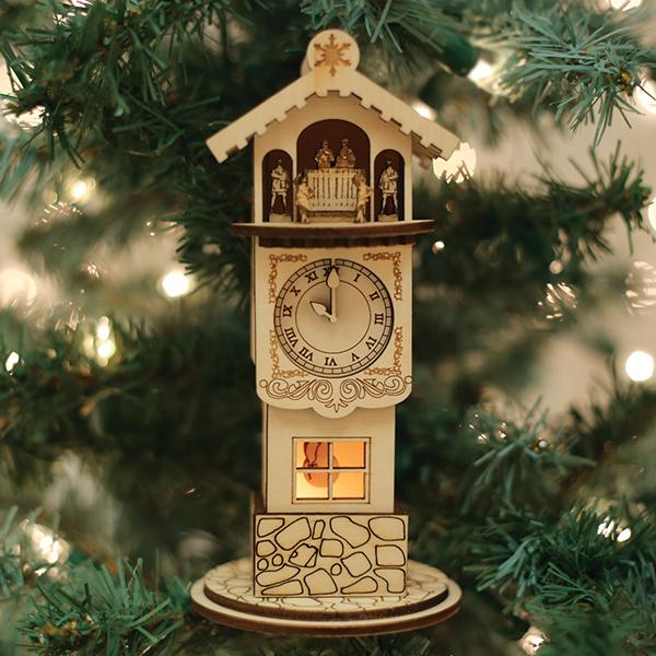 The Ginger Clock Tower Old World Christmas Ornament 80009 hangs on the tree, its wooden clock shape with Roman numerals and figurines glowing among the green branches and warm lights for a classic holiday charm.