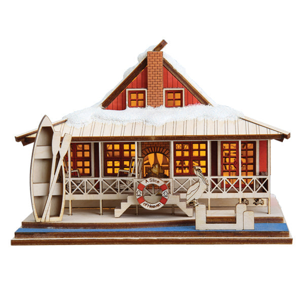 The Lake House Ornament by Old World Christmas (80046) is a miniature wooden model of Santa’s red lakeside cabin with a snowy roof, glowing windows, porch, lifebuoy, canoe, and a jumping fish by the dock.
