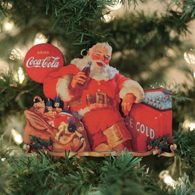 The Thirsty Santa Ornament CCO111 by Old World Christmas (84210) features Santa with a Coca-Cola bottle, sitting next to a red "ICE COLD" cooler, surrounded by toys and a Drink Coca-Cola sign—a festive addition to your Christmas tree.