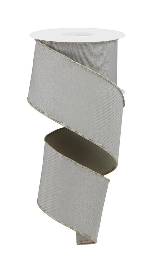 The 2.5X10Yd Diagonal Weave Fabric Taupe RGE1203LR ribbon, with a subtle sheen and stitched edges, is elegantly wound around a white cylindrical reel in a gentle spiral, highlighting its smooth diagonal weave.