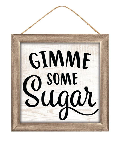 The 10Sq MDF Gimme Some Sugar Sign (AP7167) features bold black lettering on a white background with a wooden frame in light brown and beige, and hangs easily by a twine string.