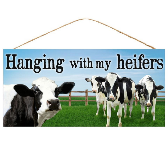 The 12.5 Hanging With My Heifer Sign (AP8720) showcases black text with Hanging With My Heifer over a scenic backdrop of five black and white cows in a grassy field, framed by a wooden fence under a blue sky.