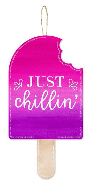 The 13.5H x 7L Just Chillin Popsicle Sign (AP8882) features hot pink, purple, tan, and white colors with a bite mark, white script text, and a top string for easy hanging.