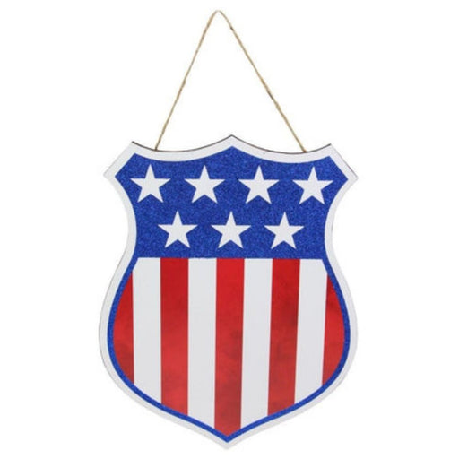 The 12H x 9.5W American Flag Badge Sign (AP8894) features a shield shape with blue glitter and white stars on top, red/white/blue vertical stripes below, and hangs from a brown string, embodying classic patriotic flair.