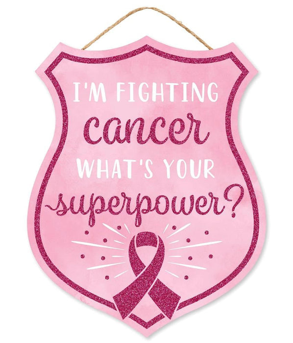 The 12H X 9.5L Fighting Cancer Badge (Product Code: AP8917) is shield-shaped, featuring Im fighting cancer. Whats your superpower? in white and hot pink on pale pink MDF, adorned with a dark pink ribbon symbol at the bottom, elegantly hung by a thin brown string.