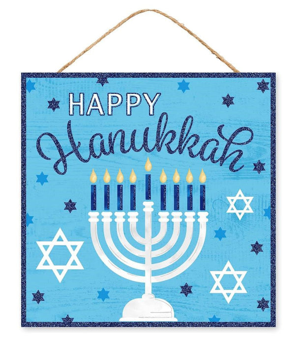 The 10Sq Happy Hanukkah Glitter Sign (AP8969) in blue, white, and light gold is made of MDF/paper, features Happy Hanukkah above a white menorah with nine lit candles and Stars of David, and hangs by twine.