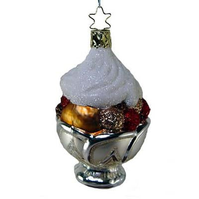 The Whipped Dream Silver Dish Ice Cream Sundae Ornament by Inge-Glas (1-024-08) is a handcrafted German ornament featuring a silver bowl, glittery toppings, white whipped cream, and a gold star hanger.