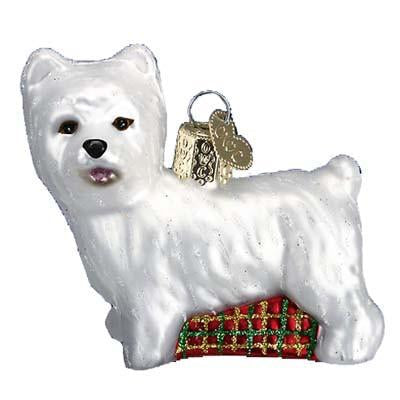 The Westie Dog 12251 Old World Christmas Ornament is a hand-painted glass decoration with a gold hanging loop, featuring a white West Highland Terrier standing on a red and green plaid cushion.