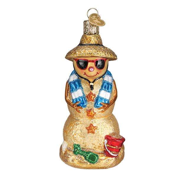 The Sand Snowman 24188 Old World Christmas Ornament by Old World Christmas is a hand-painted glass ornament featuring a straw hat, red sunglasses, blue-and-white scarf, plus a glittery red bucket with a green shovel at its base.
