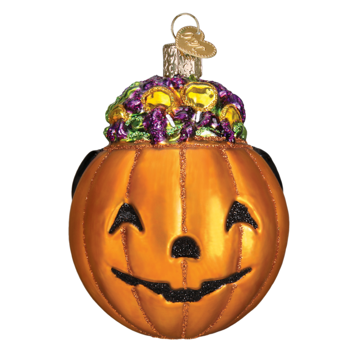 The Trick-or-Treat 26083 Old World Christmas Ornament features a shiny pumpkin with a smiling jack-o’-lantern face, topped with glittery green, purple, and yellow candies, and finished with a gold hanging loop—perfect for Halloween!.