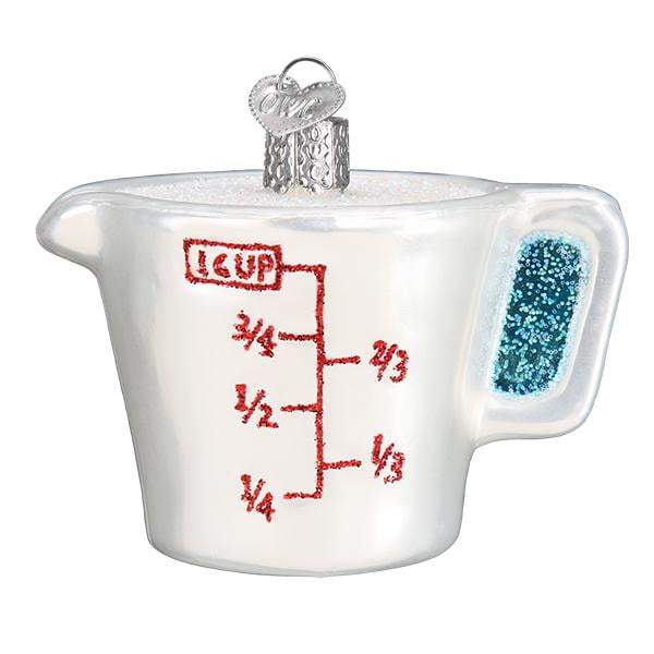 The Measuring Cup 32392 Old World Christmas Ornament is a hand-painted glass ornament shaped like a white measuring cup with red markings, a blue handle, and a silver loop for hanging.