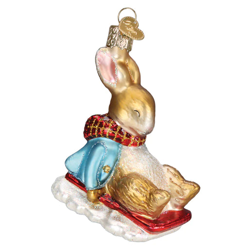 Introducing the Peter Rabbit on Sled Ornament by Old World Christmas (12688). This enchanting ornament captures the essence of a joyful bunny, similar to Peter Rabbit, riding a sled. Adorned in a blue jacket and red scarf, it brings whimsical charm to your holiday decorations. It also features a decorative loop for easy hanging on any Christmas tree.