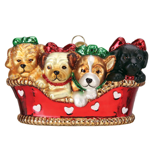 Four adorable puppies of various colors peek out from a red basket decorated with white hearts and gold trim. Resembling a scene from an Old World Christmas, these cheerful pups with their red and green bows bring about a festive and playful atmosphere, just like the Puppies in a Basket Old World Christmas 12700 ornament come to life.
