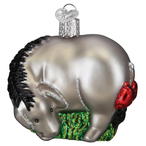 The Eeyore Old World Christmas 12704 ornament is a shiny silver donkey with a black mane and tail, adorned with a red saddle and glittery accents. It stands on a green base as a symbol of endurance and includes a silver cap for easy hanging.