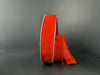 A spool of 1.5 by 10 Yard Bright Red Velvet Ribbon 131809-13 with white edges stands upright against a dark gray background, with some of the ribbon unspooled and lying to the side.