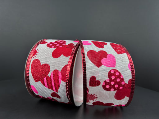 The White Linen/Red-Pink Dot Stripe Hearts ribbon, in a 2.5" width and 10-yard length, features two rolls with vibrant red and pink heart patterns on a dark gray background. It boasts a shiny finish, complemented by red edges, with the elegant touch of a subtle white linen texture.