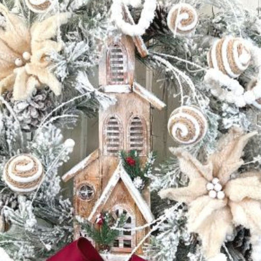 The 16 Wooden House with 5 LED Lights (84013BN) features a snowy wreath adorned with white poinsettias, pinecones, decorative swirls, frosted greenery, a red ribbon, and a central wooden house softly lit by warm LED lights.